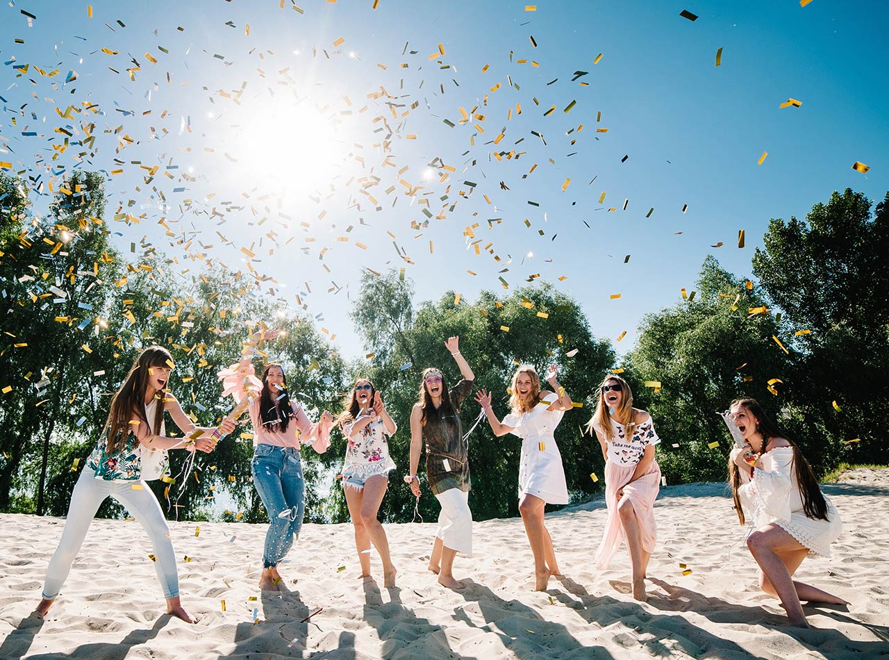 Grupo de mujeres jóvenes lanzando confeti en la playa