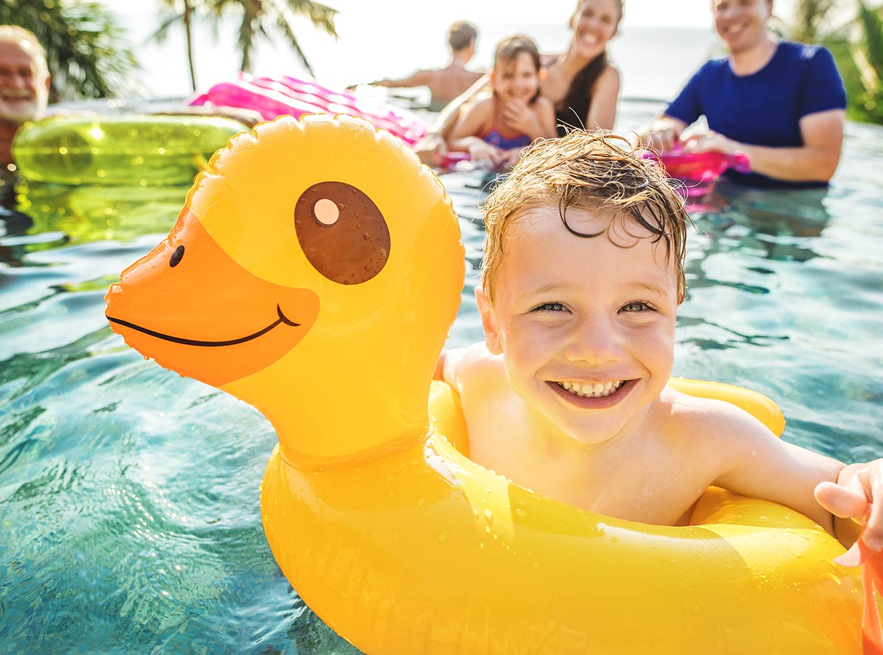 Niño nadando en la piscina del resort con la familia y la balsa de pato inflable